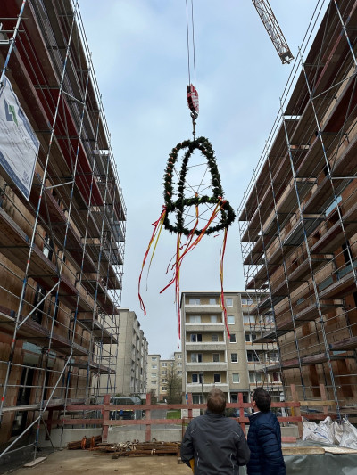 Bauherr und Bürgermeister verfolgen das Hochziehen des Richtkranzes